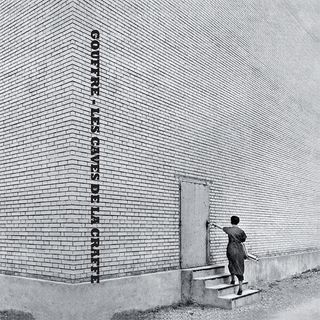 black and white picture of a girl trying to open the only door on a huge brick wall