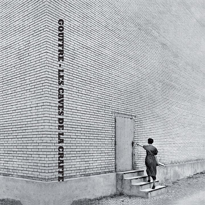 black and white picture of a girl trying to open the only door on a huge brick wall